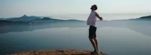 a man standing in the open air overlooking mountainous views and looking relieved