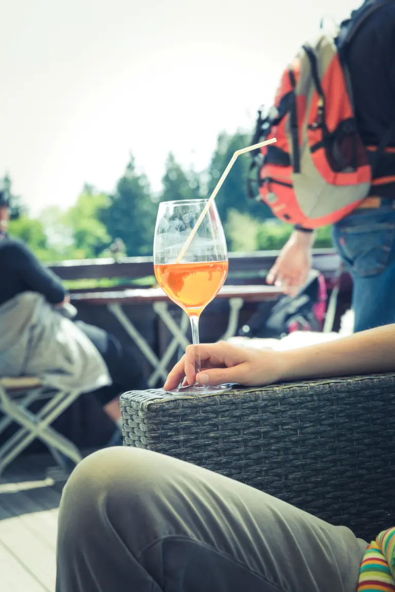 A person holding a glass of alcohol while sitting outdoors, for an article exploring can alcoholics drink casually.